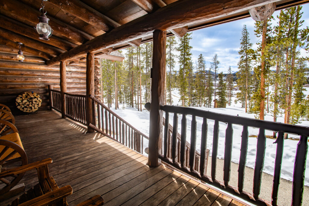 Log cabin porch with benches and log railing looking out over snowy mountain forest landscape